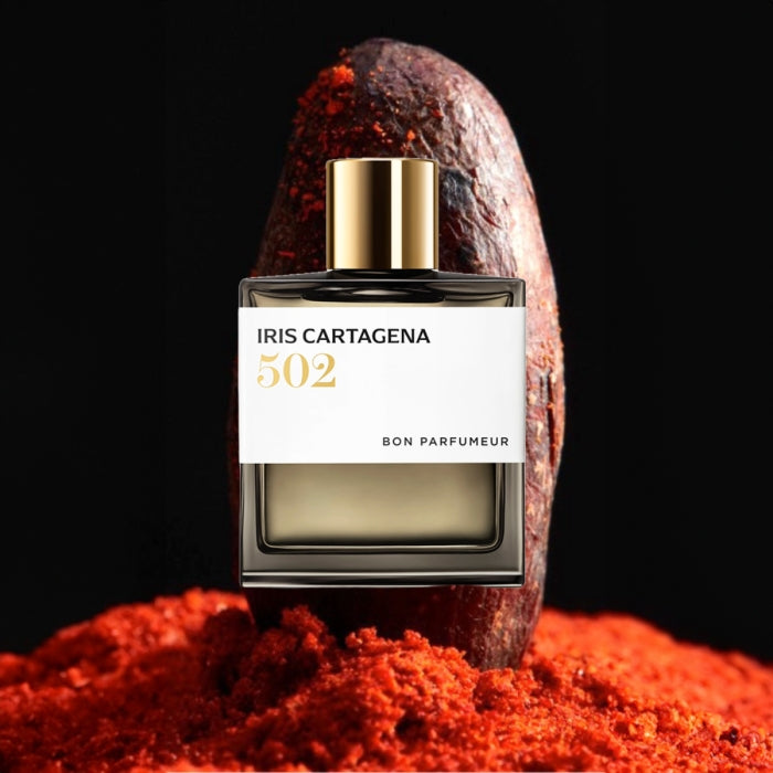 Bon Parfumeur - Les Extraits - 502 Iris Cartagena Flakon mit goldenem Verschluss vor brauner Kakaofrucht und Gewürzpulver