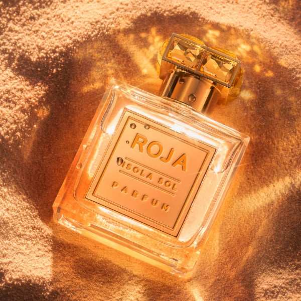 Roja Parfums - Isola Sol edler Flakon mit goldenen Details liegt im warmen Sand unter Sonneneinstrahlung