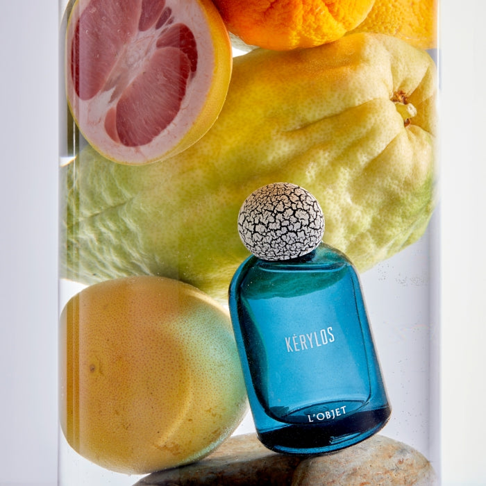 L'Objet - Kérylos Flakon in tiefblauem Glas mit weiß-rissigem Verschluss umgeben von Zitrusfrüchten frisch präsentiert
