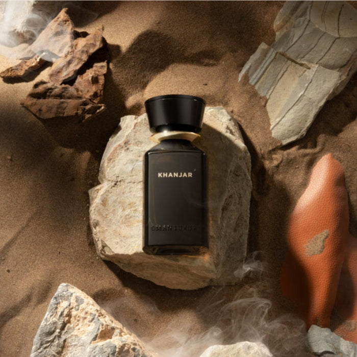Omanluxury - Khanjar Parfümflakon in tiefschwarzem Design auf felsigem Wüstenboden mit Sand und Rauch