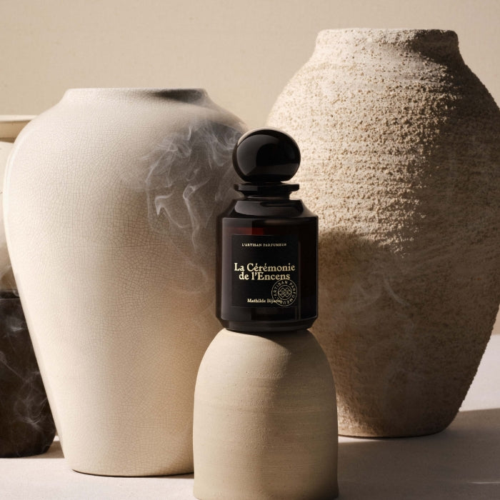 L'Artisan Parfumeur - L´Esprit du Parfum - La Cérémonie de l'Encens Flakon vor cremefarbenen Keramikvasen in natürlicher Lichtstimmung