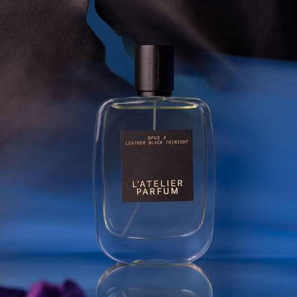 L'Atelier Parfum - Opus 2 - Leather Black (K)night klarer Flakon mit schwarzem Etikett vor blauem Hintergrund und lederner Textur
