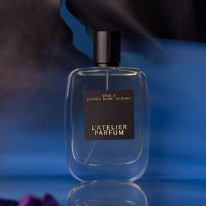 L'Atelier Parfum - Opus 2 - Leather Black (K)night klarer Flakon mit schwarzem Etikett vor blauem Hintergrund und lederner Textur