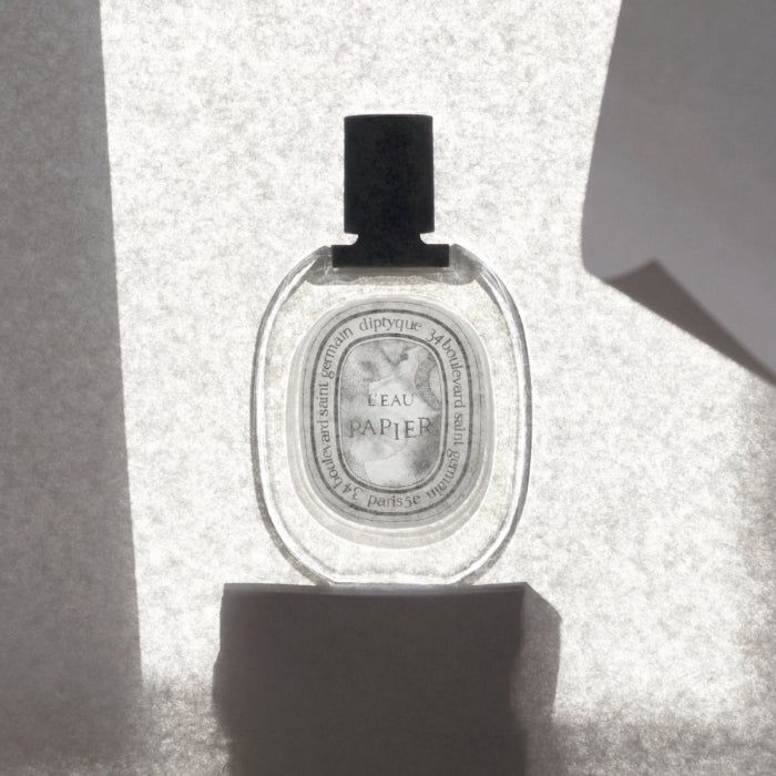 Diptyque - L'Eau Papier Parfümflakon mit klarem Glas und schwarzem Verschluss vor hellem Hintergrundlicht