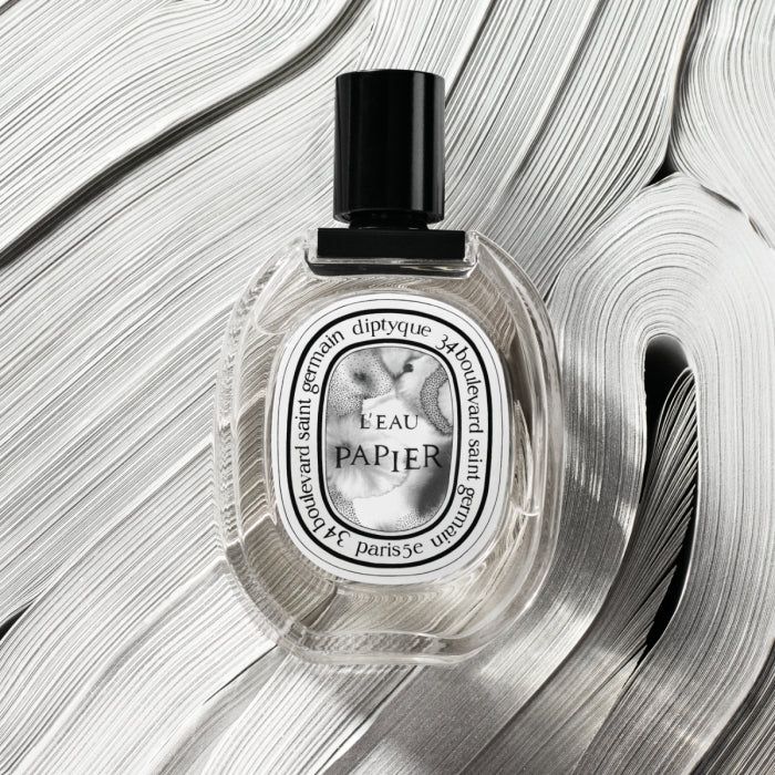 Diptyque - L'Eau Papier Parfümflakon mit schwarzem Verschluss auf skulpturalem weißem Hintergrund aus Papierrollen