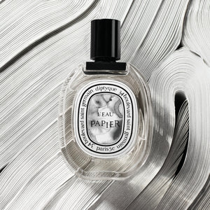Diptyque - L'Eau Papier Parfümflakon mit schwarzem Verschluss auf skulpturalem weißem Hintergrund aus Papierrollen