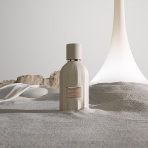Amouage - Essences Collection - Lustre zeigt cremefarbenen Flakon mit zartem Rosé-Label vor sanft strukturierter Oberfläche