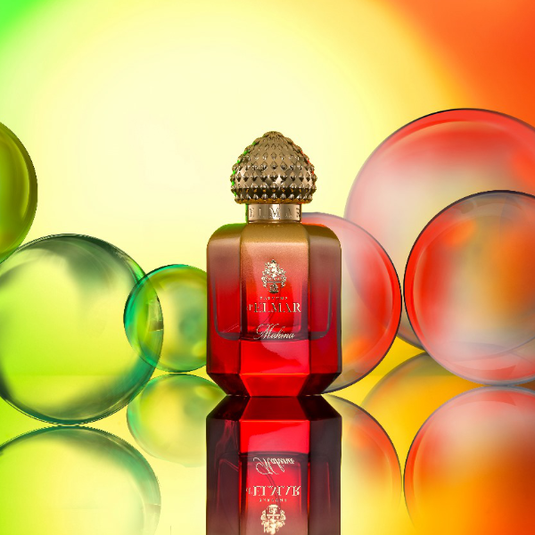 Parfums d'Elmar - Mahina Parfümflakon in leuchtendem Rot mit kunstvoll strukturiertem, rundem Verschluss vor farbigen Kugeln