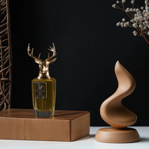 Pana Dora Sweden - Majestic Amber Parfumflakon mit goldenem Hirschkopf auf Holzpodest vor dunklem Hintergrund