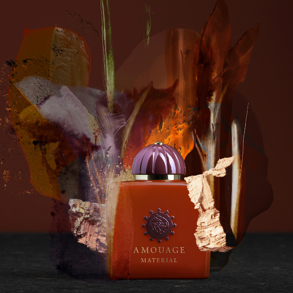 Amouage - Material Parfumflakon in kräftigem Orange mit violettem Deckel und goldfarbenem Logo vor dunklem künstlerischem Hintergrund