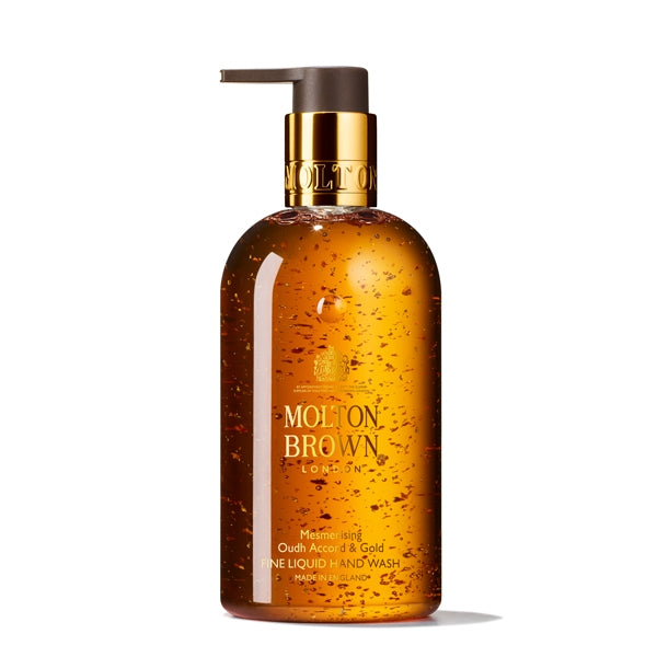 Molton Brown - Mesmerising Oudh Accord & Gold Fine Liquid Hand Wash bernsteinfarbener Spender mit goldfarbenem Verschluss vor weißem Hintergrund
