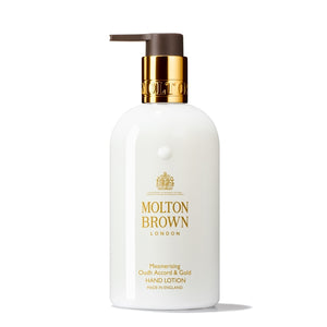 Molton Brown - Mesmerising Oudh Accord & Gold Hand Lotion weiße Flasche mit goldfarbenem Verschluss und braunem Pumpspender vor weißem Hintergrund