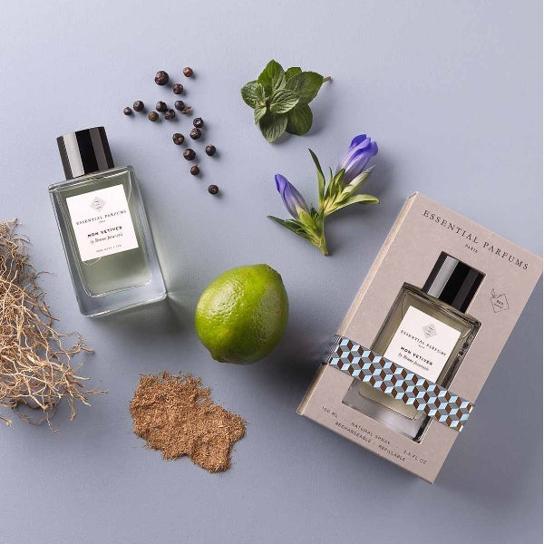 Essential Parfums - Mon Vetiver Flakon mit schwarzem Deckel neben Naturmaterialien und Verpackung auf hellgrauem Untergrund