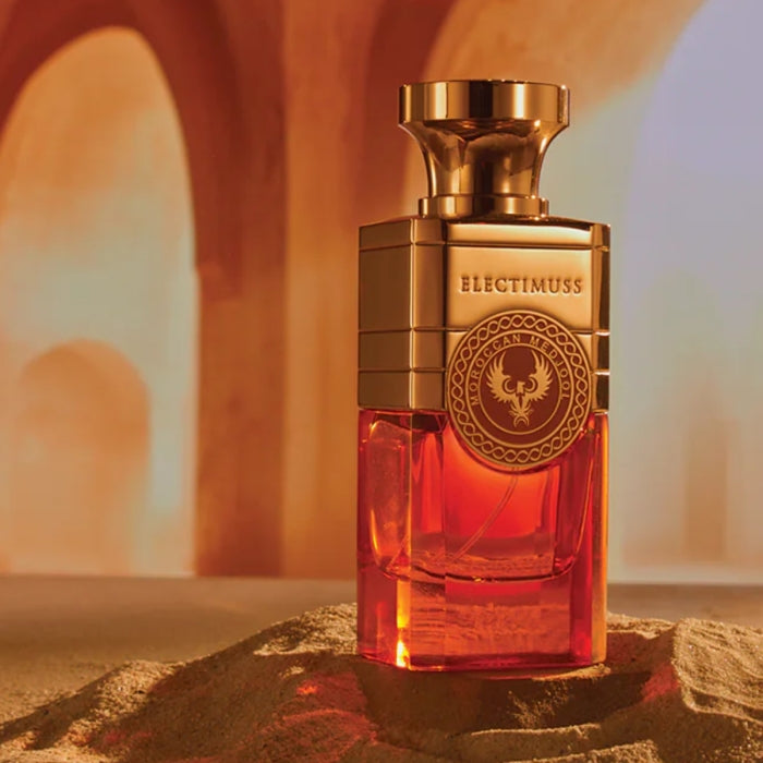 Electimuss - Moroccan Medjool Parfumflakon mit goldfarbenem Oberteil und warm leuchtendem, bernsteinfarbenem Glas in Wüstenkulisse