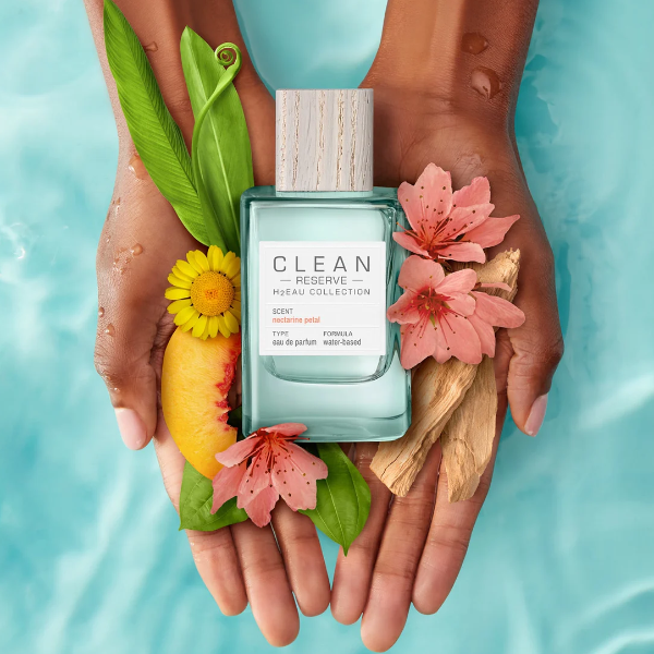 Clean Perfume - H2Eau Nectarine Petal Parfümflakon mit Holzverschluss, Pfirsich- und Blütenarrangement auf Händen vor Wasserhintergrund
