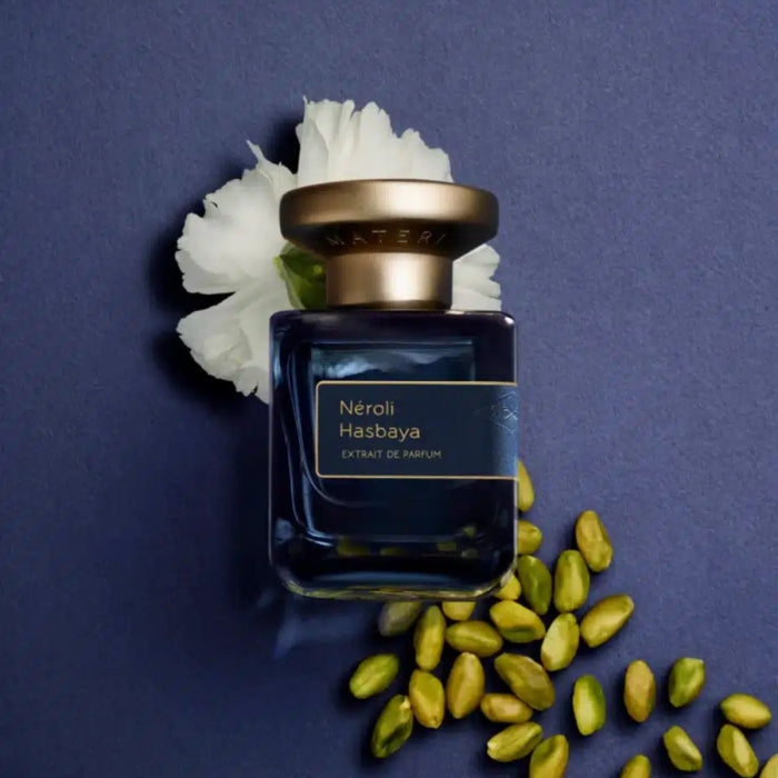Atelier Materi - Néroli Hasbaya Parfumflakon in tiefblauem Glas mit goldfarbenem Verschluss vor lila Hintergrund