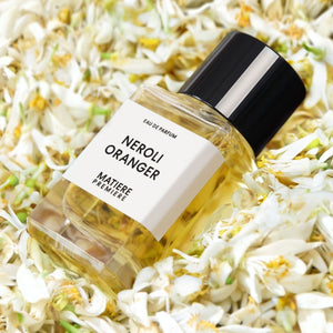 Matière Première - Neroli Oranger zeigt klaren Flakon mit hellem Parfum vor Blüten der Orangenblüte