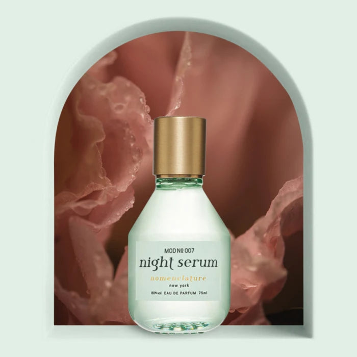 Nomenclature - night serum Glasflakon mit matter grüner Hülle und goldfarbenem Verschluss vor zart rosafarbener Blüte