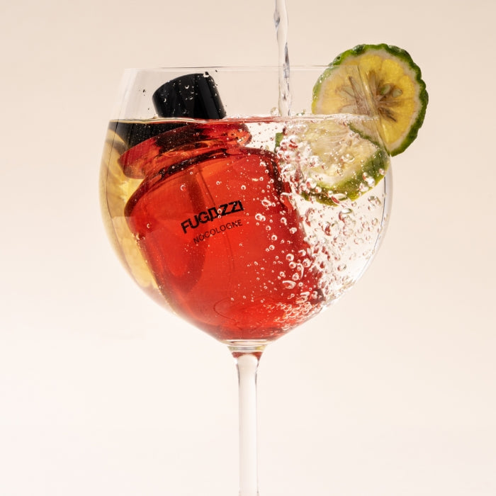 Fugazzi - Nocologne roter Flakon in Glas mit kohlensäurehaltigem Sprudelwasser und einer Limettenscheibe am Glasrand