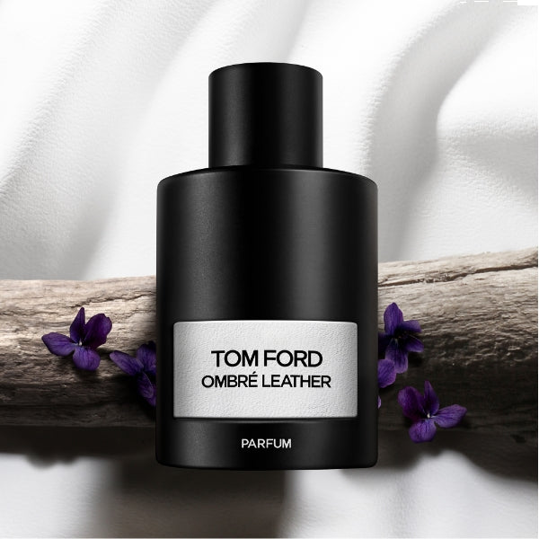 Tom Ford - Signature - Ombre Leather - Parfum schwarzer Flakon mit silbernem Etikett vor Holz und violetten Blüten