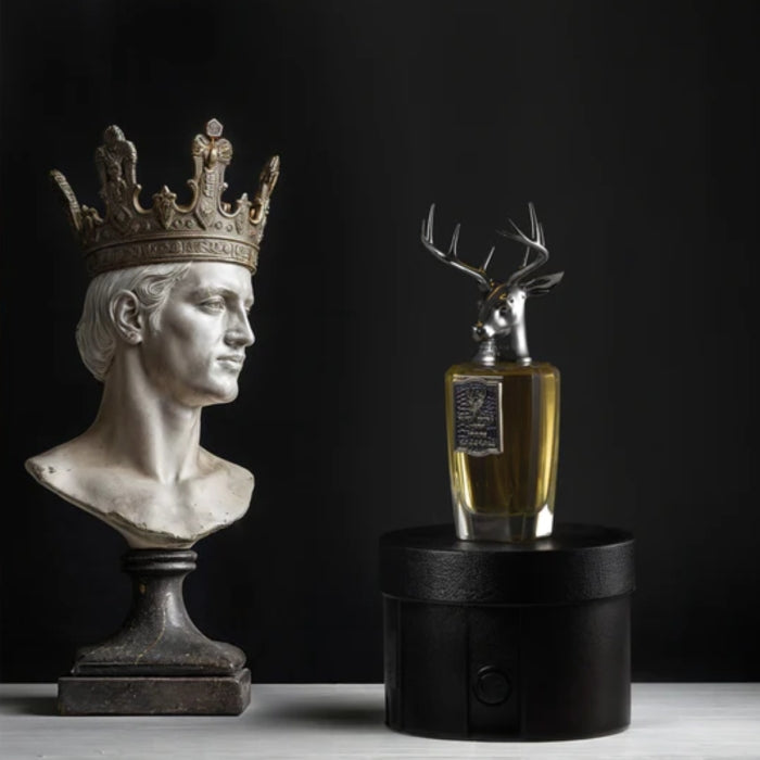 Pana Dora Sweden - Opuluxe Parfumflakon mit silbernem Hirschkopf auf rundem schwarzen Podest neben antiker Büste mit Krone