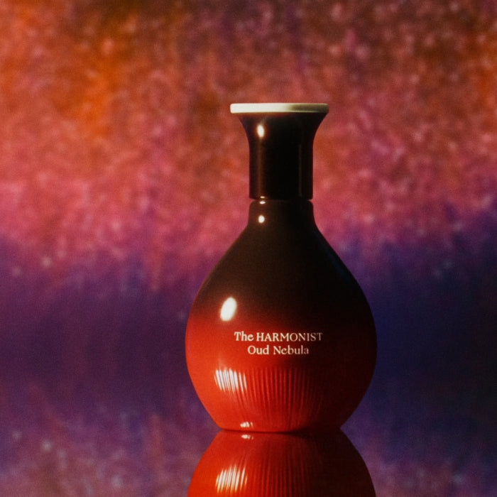 The Harmonist - Oud Nebula Flakon in rundem Design mit warmem Farbverlauf vor abstraktem, leuchtendem Hintergrund