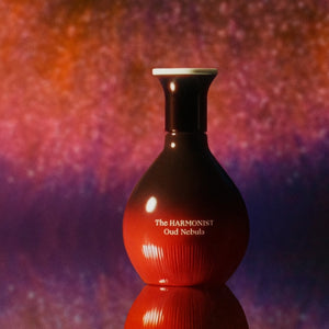 The Harmonist - Oud Nebula Flakon in rundem Design mit warmem Farbverlauf vor abstraktem, leuchtendem Hintergrund