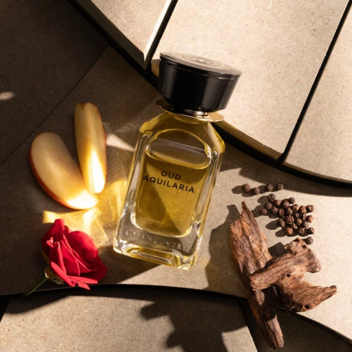 Omanluxury - Oud Aquilaria Parfümflakon mit goldfarbenem Duft umgeben von Apfel, Rose und harzigen Holznoten auf Steinfläche
