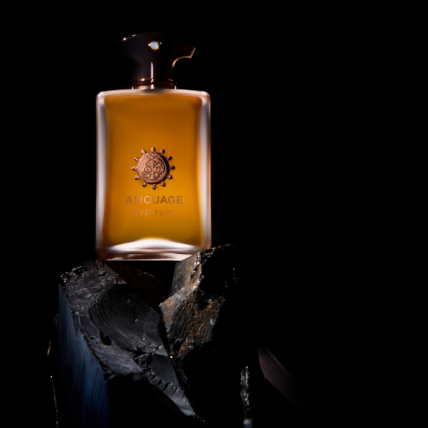 Amouage - Overture Man Parfumflakon mit kupferfarbenem Verschluss auf dunklem Untergrund und schwarzem Stein