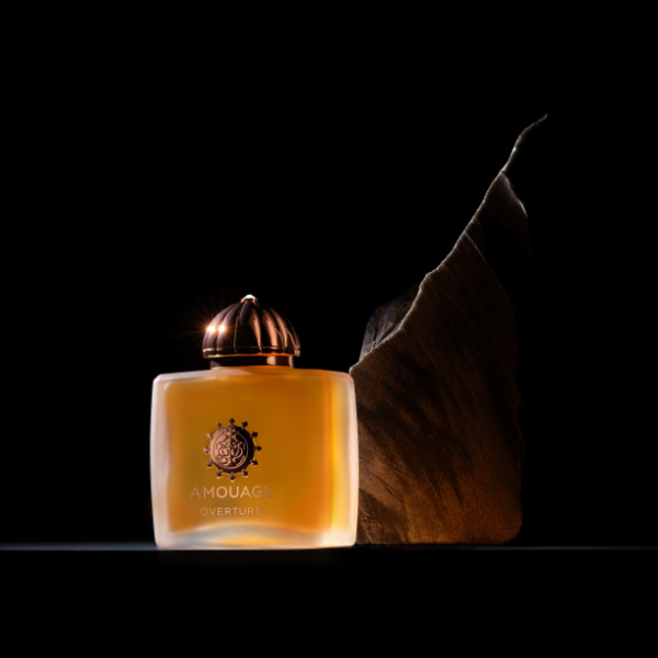 Amouage - Overture Woman Parfumflakon mit kupferfarbenem Verschluss vor dunklem Hintergrund und Stein-Dekor