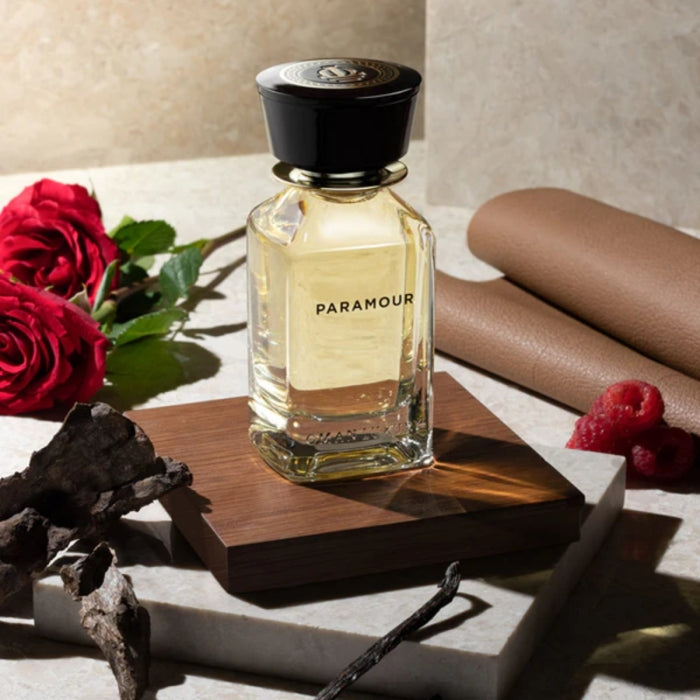 Omanluxury - Paramour Parfümflakon mit bernsteinfarbenem Duft, umgeben von roten Rosen und Holz auf Marmorfläche