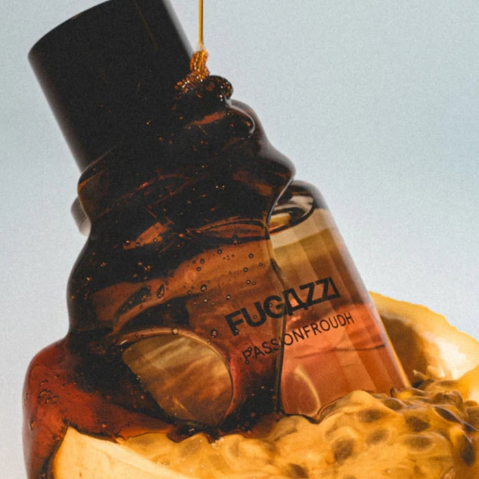 Fugazzi - Passionfroudh zeigt bernsteinfarbenen Flakon mit honigartigem Überzug und Maracuja-Früchten im Hintergrund