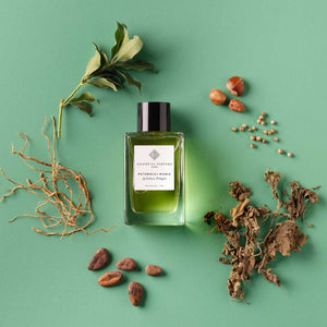 Essential Parfums - Patchouli Mania grüner Flakon mit schwarzem Deckel und verschiedenen Naturstoffen auf grünem Hintergrund