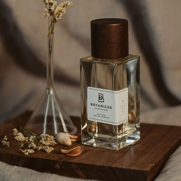 Botanicae - Patio Parfumflakon mit klarem Glas und dunkelbraunem Holzverschluss auf Holzunterlage mit getrockneten Blumen