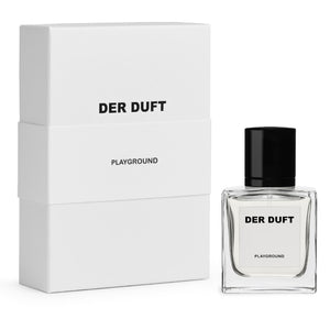 DER DUFT - Playground Parfumflakon mit klarem, eckigem Design und schwarzem Verschluss neben passender, schlichter Verpackung