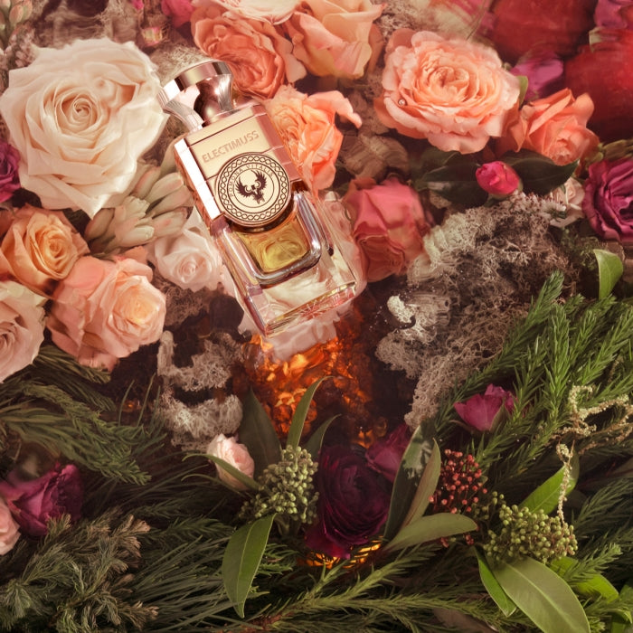 Electimuss - Pomona Vitalis Flakon umgeben von Rosen und grünen Pflanzenelementen in warmer, natürlicher Atmosphäre