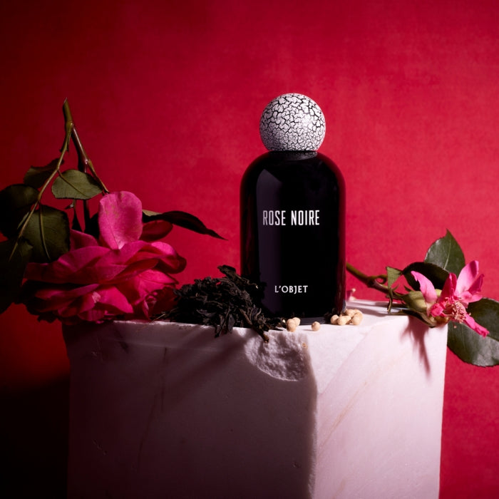 L'Objet - Rose Noire Parfumflakon in schwarzem Glas mit auffälligem weiß-rissigem Verschluss vor rotem Hintergrund