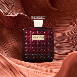 Houbigant - Collection les Ambres - Rose du Desert Parfumflakon in tiefrotem Design mit geprägtem Muster vor Wüstenhintergrund