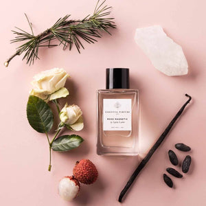 Essential Parfums - Rose Magnetic Flakon mit schwarzem Deckel umgeben von Naturstoffen auf rosafarbenem Untergrund