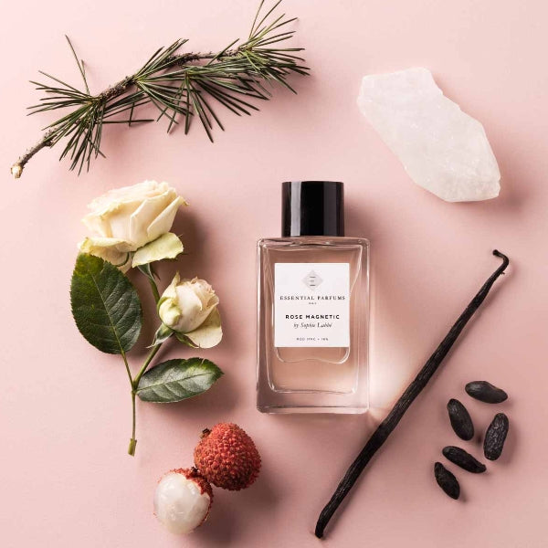 Essential Parfums - Rose Magnetic Flakon mit schwarzem Deckel umgeben von Naturstoffen auf rosafarbenem Untergrund