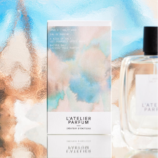 L'Atelier Parfum - Opus 3 - Salty Wood Verpackung mit zarten Aquarellfarben vor glänzendem Hintergrund
