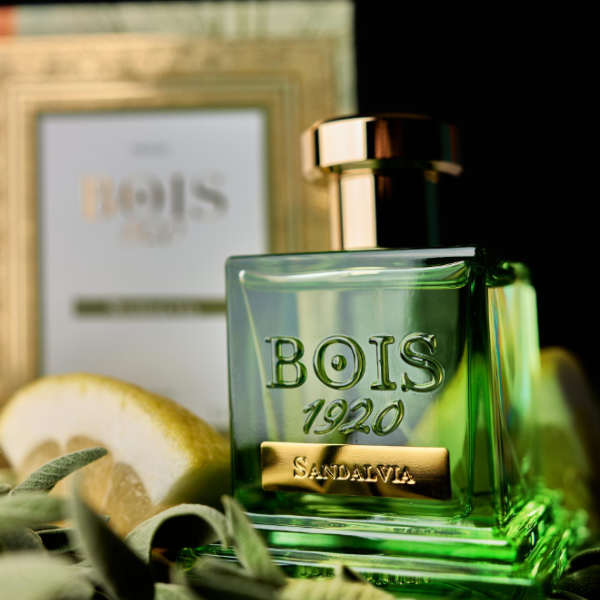 Bois 1920 - Sandalvia Flakon in grünlich-transparent mit goldfarbenem Verschluss und Zitrusakzenten vor dunklem Hintergrund