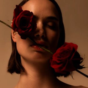 Mihan Aromatics - Sinful Rose Nahaufnahme einer Frau mit geschlossenen Augen und roten Rosen vor beigem Hintergrund