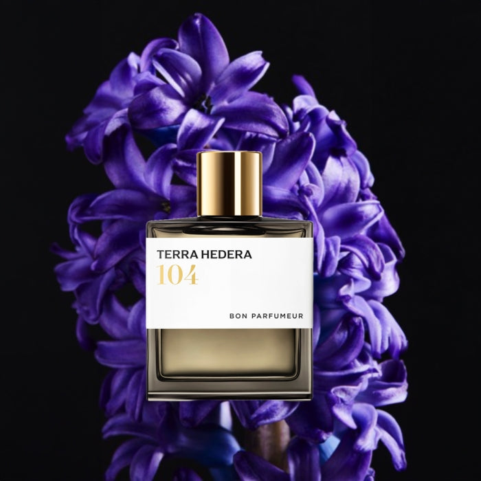 Bon Parfumeur - Les Extraits - 104 Terra Hedera Flakon mit goldfarbenem Verschluss vor violetten Hyazinthen vor schwarzem Hintergrund