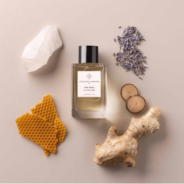 Essential Parfums - The Musc Flakon mit schwarzem Verschluss umgeben von Ingwer, Lavendelblüten, Holzscheiben und Bienenwachs