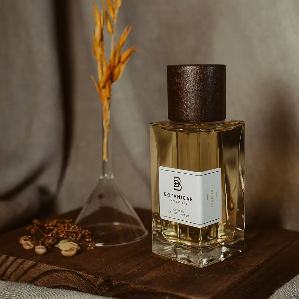 Botanicae - Tramonte Parfumflakon mit honigfarbenem Duft und dunklem Holzverschluss auf Holzbrett vor Stoffhintergrund