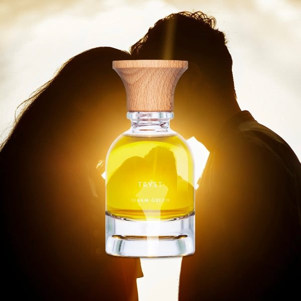 Hiram Green - Tryst Parfumflakon mit klarem Glas und hellem Holzdeckel vor romantischem Sonnenuntergangsschatten