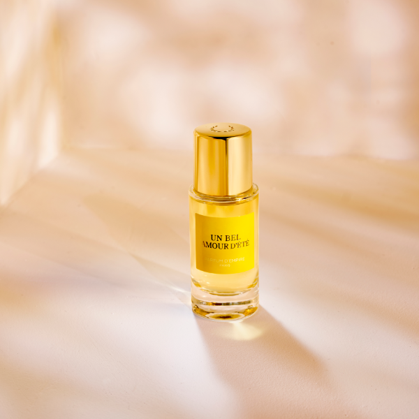 Parfum d'Empire - Un Bel Amour d’Été Flakon mit goldenem Verschluss vor warm leuchtendem, sanft texturiertem Hintergrund
