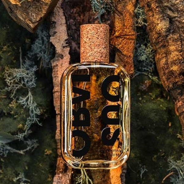 Obvious - Un Patchouli Flakon mit klarem Glas, Korkverschluss und kräftiger schwarzer Schrift vor Naturhintergrund