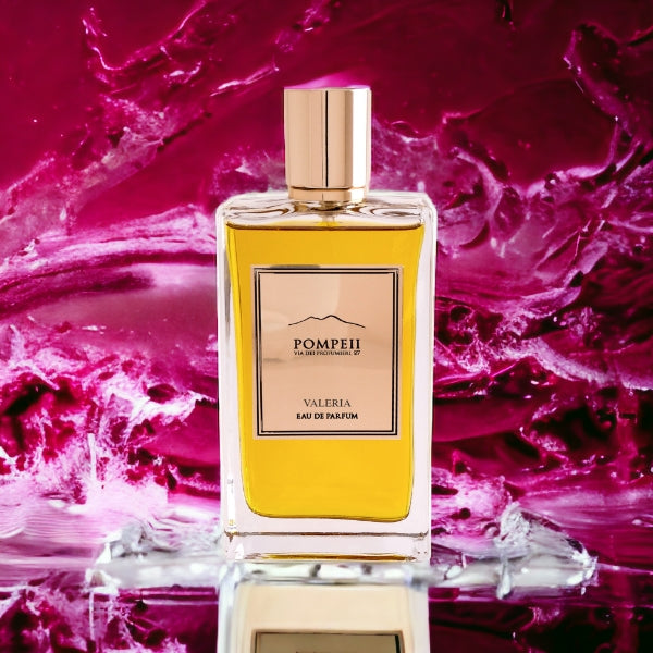 Pompeii - Valeria Parfumflakon mit goldfarbenem Verschluss und bernsteinfarbenem Duft vor pink-rotem Aquarellhintergrund